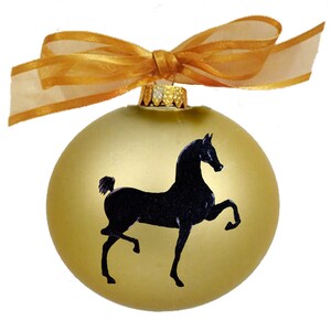 May include: A gold Christmas ornament with a black silhouette of a horse. The ornament is tied with a gold ribbon.