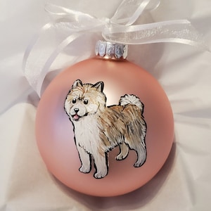 May include: A hand-painted Christmas ornament featuring a brown and white dog on a blush pink background.