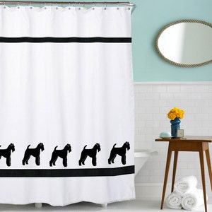 May include: White shower curtain with a black border and a row of black silhouette images of dogs at the bottom. The shower curtain is hanging in a bathroom with white tile walls and a brown wooden table with a vase of yellow flowers.