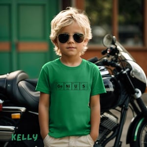 May include: A young boy wearing a green t-shirt with the word "GENIUS" spelled out using chemical element symbols. He is wearing sunglasses and standing in front of a motorbike.