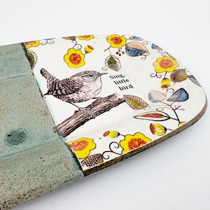May include: A ceramic serving platter with a bird illustration and the text "Sing, little bird." The platter features a gray textured section and a white section with yellow flowers and leaves. The bird is perched on a branch.