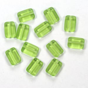 May include: A collection of translucent, light green rectangular beads with a white stripe detail. The beads are scattered on a white surface, showcasing their shape and color. These beads are suitable for jewelry making and crafting projects.