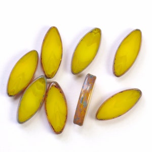 May include: Eight yellow glass beads with a slightly iridescent finish. The beads are oval shaped and have a slightly irregular edge.