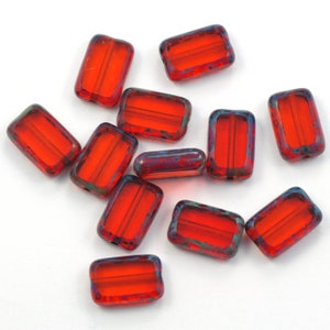 May include: A group of red glass beads with a blue iridescent finish. The beads are rectangular in shape with a hole in the center.