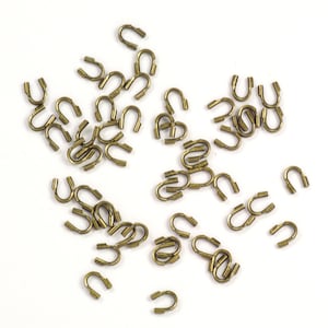 May include: A large quantity of small, gold-colored metal loops. The loops are all the same size and shape, and they are scattered randomly on a white surface.