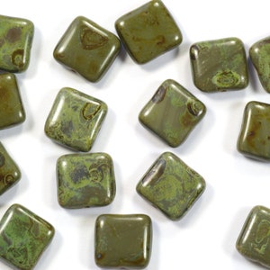 May include: A collection of 14 square green glass beads with brown marbling. The beads are scattered on a white surface.