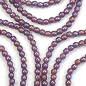May include: Strands of iridescent purple beads. The beads have an oval shape and a glossy finish, with hints of blue and gold. The beads are strung together, creating a flowing, elegant look. Ideal for jewelry making or craft projects.