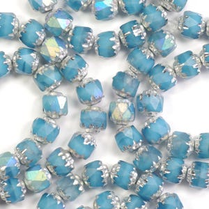 May include: Close-up of light blue faceted beads with silver-colored metal accents. The beads have an iridescent sheen and are strung together. The beads are likely for jewelry making or crafting.