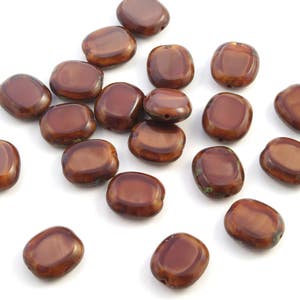 May include: A collection of 18 brown glass beads with a slightly iridescent finish. The beads are oval shaped and have a smooth, polished surface.