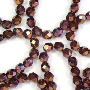 May include: Close-up of faceted, iridescent beads in shades of brown, gold, and purple. The beads are strung together, creating a necklace or bracelet design. The beads have a geometric shape and a shiny finish.