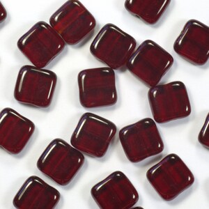May include: A scattering of small, square, red glass beads. The beads have a slightly irregular shape and a glossy finish.