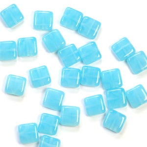 Könnte beinhalten: Eine Streuung von hellblauen quadratischen Glasfliesen mit weißen Wirbeln. Die Fliesen sind auf einem weißen Hintergrund verstreut.