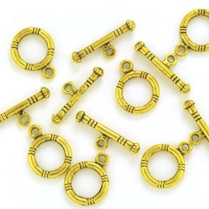 May include: A set of ten gold-toned metal toggle clasps for jewelry making. Each clasp features a round ring with a decorative design and a straight bar with a small loop at each end.