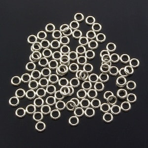 May include: A large pile of silver jump rings. The rings are small and round, and they are all the same size.