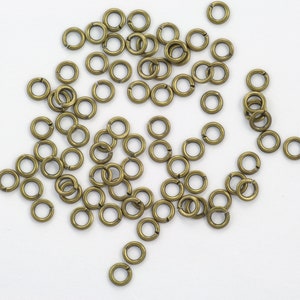May include: A large quantity of small, gold-colored jump rings. The rings are scattered on a white surface.