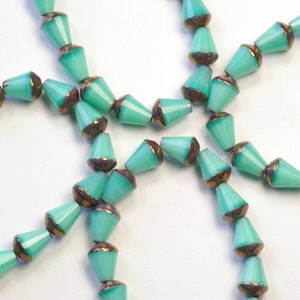 May include: A strand of turquoise blue glass beads with gold accents. The beads are faceted and have a pointed shape.