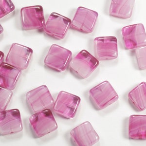 May include: A collection of pink square glass beads with white swirls. The beads are translucent and have a glossy finish.