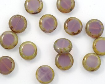 May include: A collection of flat, round beads with a central lavender-purple disc surrounded by a golden-green rim. The beads are scattered on a white surface, showcasing their iridescent quality. These beads are ideal for jewelry making.