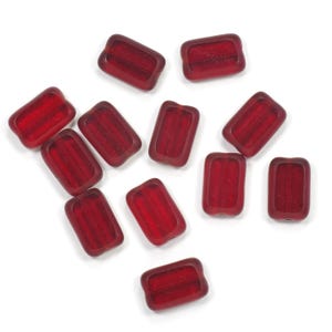 May include: A collection of eleven rectangular glass beads in a deep red hue. Each bead features a smooth, matte-finished border surrounding a slightly recessed, textured center panel with a horizontal channel running through the middle.