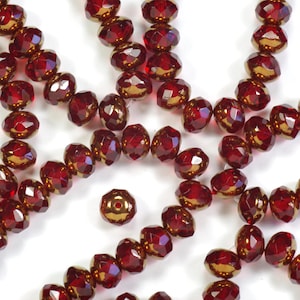 May include: Close-up of faceted, deep red beads with a golden luster. The beads are strung together, showcasing their multi-faceted surfaces. The beads are likely for jewelry making or crafting.
