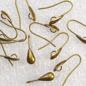 May include: A group of gold-toned earring hooks with a teardrop shape. The hooks are made of metal and have a smooth finish.