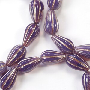 Puede incluir: Una hebra de cuentas de vidrio púrpura con acentos dorados. Las cuentas tienen forma de lágrima y una superficie texturizada.