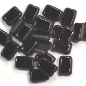 May include: A pile of black glass rectangular beads. The beads are smooth and shiny.