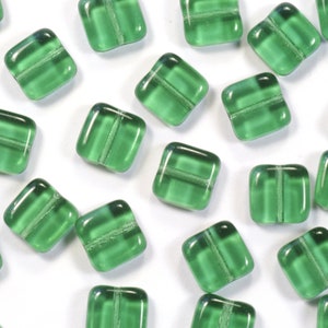 Può includere: Una dispersione di perline quadrate di vetro verde con una linea centrale trasparente. Le perline sono su uno sfondo bianco.