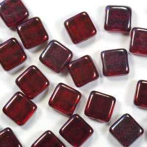 May include: A scattering of small, square, red glass beads with a subtle iridescent sheen.