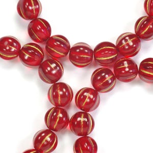 May include: Close-up of red glass beads with gold stripes. The beads are round and have a glossy finish. The gold stripes are evenly spaced around the circumference of each bead. The beads are strung together, creating a necklace or bracelet.