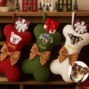 Könnte beinhalten: Drei weihnachtliche Strümpfe in Knochenform in Rot, Grün und Weiß, jeweils mit einem Hundeporträt und Namen: Bentley, Kodi und Mochi. Sie haben eine Schleife und eine kleine Geschenkbox. Festliche Dekoration.