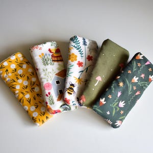 May include: Five rectangular fabric items with various patterns. Designs include yellow with white flowers, a farmhouse scene, floral with a bee, green with mushrooms, and dark green with flowers. The items are arranged on a white surface.