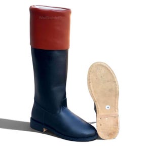 May include: A tall black boot with a folded-over brown cuff at the top. The boot features a smooth black shaft and a rounded toe. Beside it, the light-colored sole of the boot is visible, displaying a white sticker with the number 10.