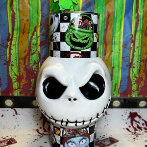 May include: A white Jack Skellington-themed container with a black and white checkered pattern and images of characters from The Nightmare Before Christmas. A green Oogie Boogie figure sits on top.