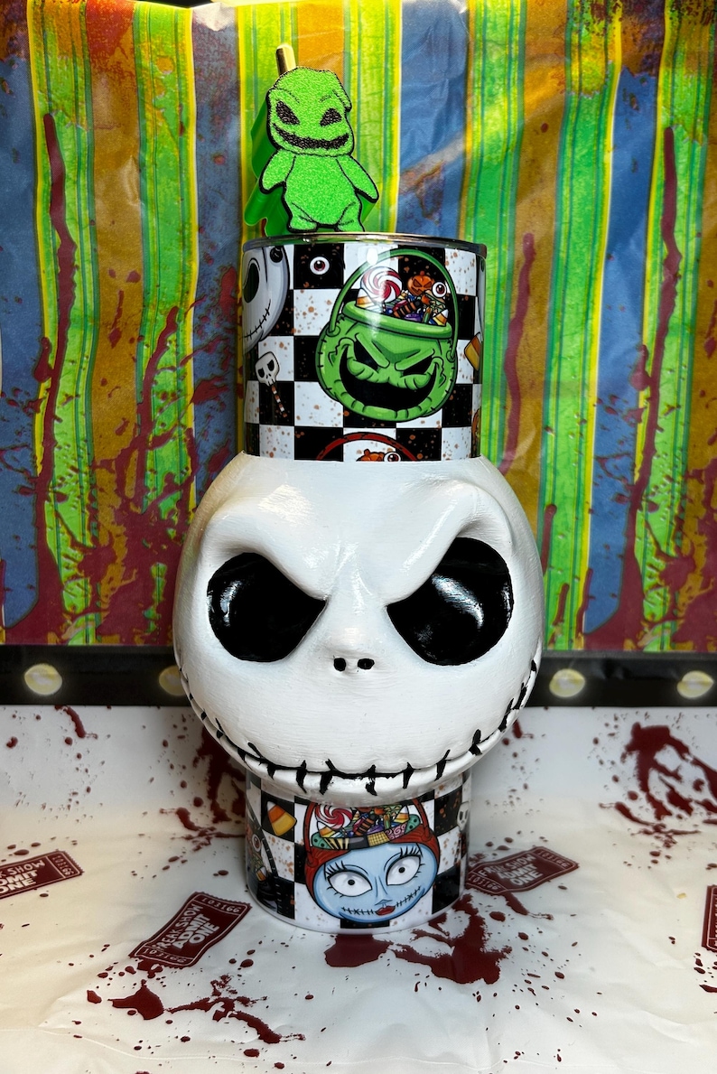 May include: A white Jack Skellington-themed container with a black and white checkered pattern and images of characters from The Nightmare Before Christmas. A green Oogie Boogie figure sits on top.