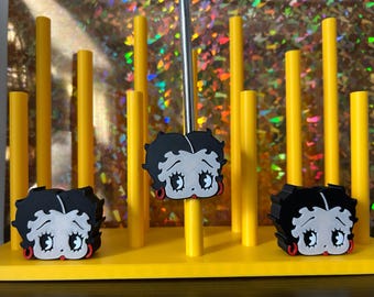 May include: A yellow display stand with three Betty Boop character figures. The figures are black, white, and red. The stand has yellow vertical poles and a reflective background.