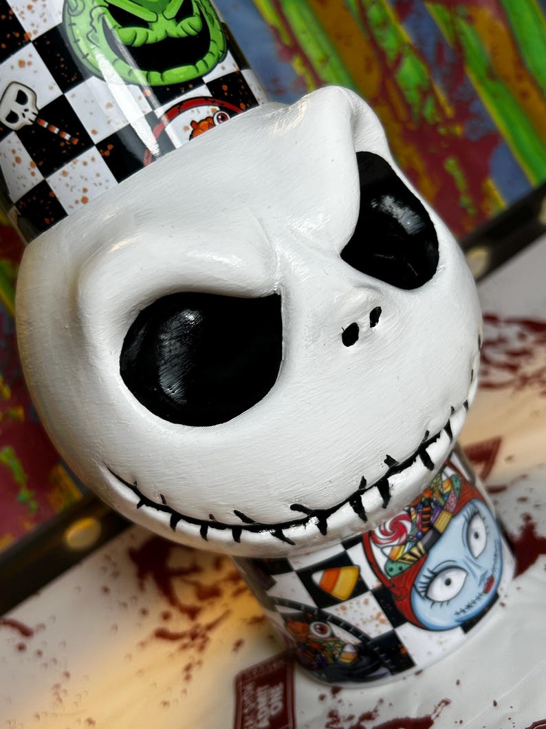 May include: A white, hand-painted Jack Skellington figurine from The Nightmare Before Christmas. The figurine features a stitched mouth, black eye sockets, and a checkered pattern with other characters. The base has a Sally illustration.