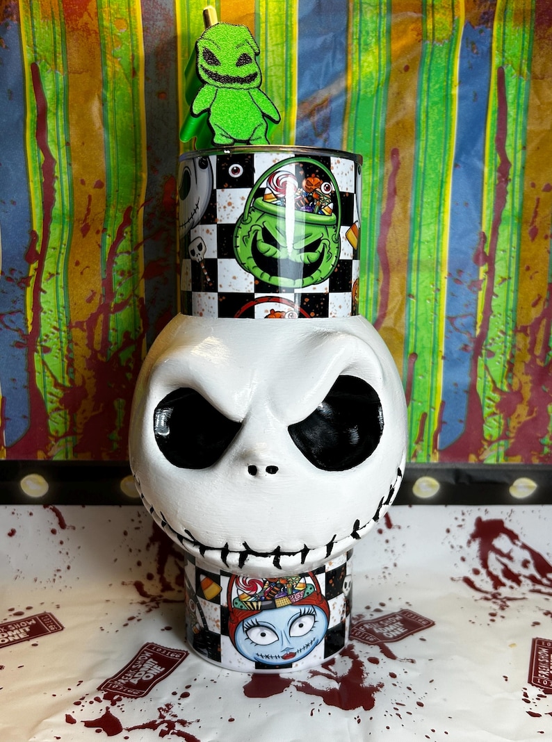 May include: A white ceramic Jack Skellington head with black eyes and stitched mouth. A cylindrical container with a checkered pattern and Oogie Boogie and Sally designs sits on top. A green Oogie Boogie figure is on top.