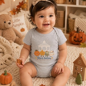 Könnte beinhalten: Ein hellgrauer kurzärmeliger Babybody mit einer Grafik aus einem weißen Pavillon, einem lächelnden Kürbis, einem Blatt, einem Buch und einer Tasse Kakao sowie dem in Blau und Orange gedruckten Text Stars Hollow und Little Autumn Friends.