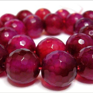 Op de afbeelding: Een streng ronde, gefacetteerde, diep roze agaat kralen. De kralen zijn geregen op een doorzichtige draad en hebben een gepolijste, glanzende afwerking.