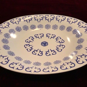 May include: Oval serving platter with a white base and a blue floral design. The rim features a repeating pattern of stylized flowers and scrollwork. The center has a similar design. A decorative piece for serving food.