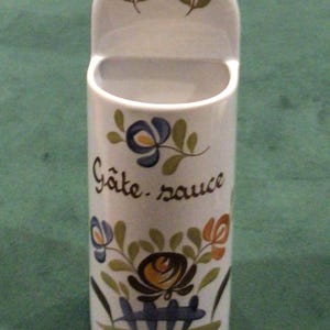 May include: White ceramic wall-mounted container with a floral design and the text "Gâte sauce".