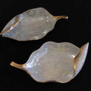 May include: Two white ceramic leaf-shaped dishes with gold trim. The dishes have an iridescent finish.