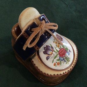 May include: A ceramic shoe shaped trinket with a blue and white floral design. The shoe has a brown leather lace and a brown base.