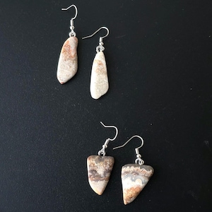 Puede incluir: Cuatro pares de pendientes de piedra con ganchos plateados. Los pendientes tienen una forma natural y org&aacute;nica y presentan una mezcla de tonos beige, marr&oacute;n y blanco. Los pendientes se muestran sobre una superficie negra.
