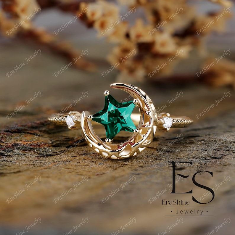 K&ouml;nnte beinhalten: Ein goldener Ring mit einem Halbmond-Design und einem gr&uuml;nen sternf&ouml;rmigen Edelstein. Der Ring hat einen kleinen Diamanten-Akzent an der Seite.