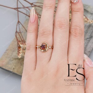 K&ouml;nnte beinhalten: Ein goldener Ring mit einem Halbmond-Design und einem roten Edelstein in der Mitte. Der Ring ist mit kleinen wei&szlig;en Edelsteinen auf beiden Seiten des roten Edelsteins besetzt. Der Ring befindet sich an einem Finger.