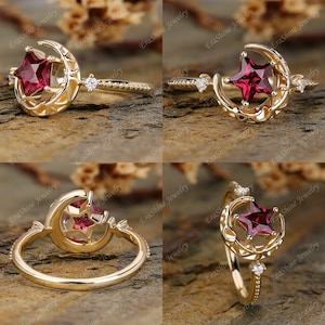 K&ouml;nnte beinhalten: Ein goldener Ring mit einem Halbmond-Design und einem roten Edelstein, der in eine Sternform gefasst ist. Der Ring ist mit kleinen Diamanten verziert.