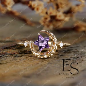K&ouml;nnte beinhalten: Ein goldener Ring mit einem Halbmond-Design und einem lila sternf&ouml;rmigen Edelstein. Der Ring ist mit kleinen Diamanten auf der Band besetzt.