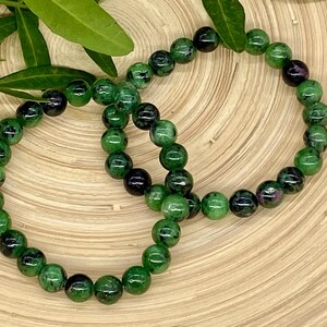 Könnte beinhalten: Zwei grüne und schwarze Edelstein-Armbänder mit runden Perlen. Die Armbänder sind aus natürlichen Steinen gefertigt und übereinander gelegt.